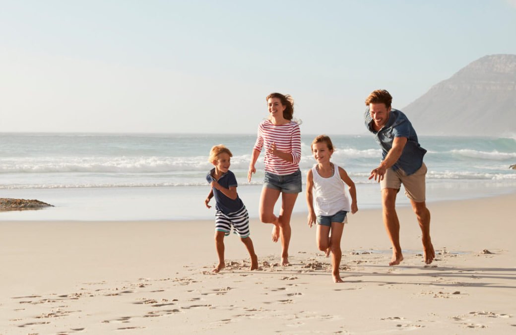 Parents Running Along Beach With Children On Summer Vacation